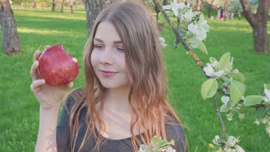 güzel genç kadın bir elma bir elma bahçesi zemin karşı onun elinde. Bir kadın bir elma yiyor. Bahçe çiçek açan bir bahçeye sahip. Meyve ağaçları çiçekleri.