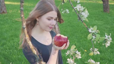 güzel genç kadın bir elma bir elma bahçesi zemin karşı onun elinde. Bir kadın bir elma yiyor. Bahçe çiçek açan bir bahçeye sahip. Meyve ağaçları çiçekleri.