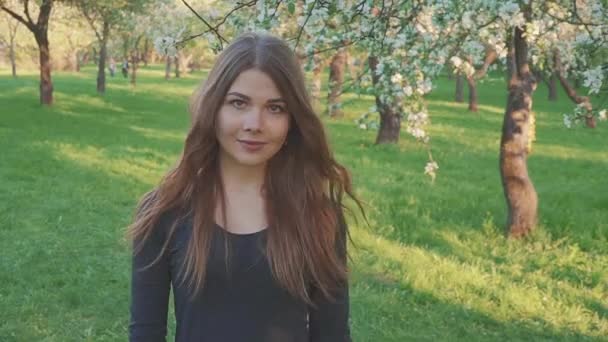 Mujer joven caminando en un huerto de manzanas en las flores de primavera blanco. Retrato de una hermosa niña en el jardín de frutas de la noche . — Vídeo de stock