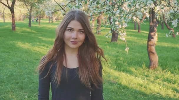 Jonge vrouw lopen in een appelboomgaard in de Lentebloemen wit. Portret van een mooi meisje in de avond groente tuin. — Stockvideo