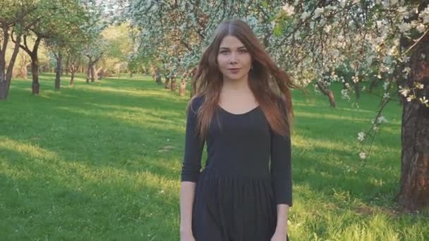 Jonge vrouw lopen in een appelboomgaard in de Lentebloemen wit. Portret van een mooi meisje in de avond groente tuin. — Stockvideo