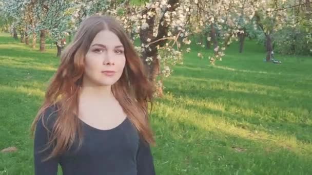 Ung kvinna promenader i en äppelodling i de vita vårblommorna. Porträtt av en vacker flicka i kväll fruktträdgård. — Stockvideo