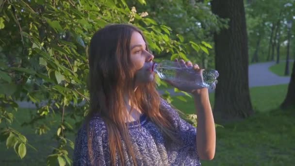 Belle randonneuse qui boit de l'eau en forêt au coucher du soleil. Une fille en robe boit de l'eau fraîche d'une bouteille en plastique . — Video
