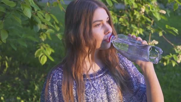 Prachtige vrouwelijke wandelaar drinkwater in bos bij zonsondergang. Een meisje in een jurk drinkt cool water uit een plastic fles. — Stockvideo