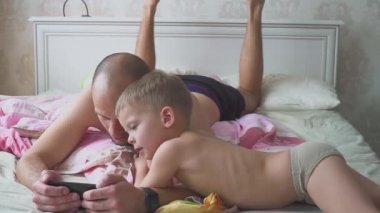 Baba ve oğlu yatakta yatarken ve cep telefonuyla birlikte