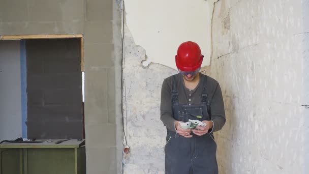 De werknemer in een constructie met helm telt geld euro tegen de achtergrond van het gerepareerde appartement. — Stockvideo