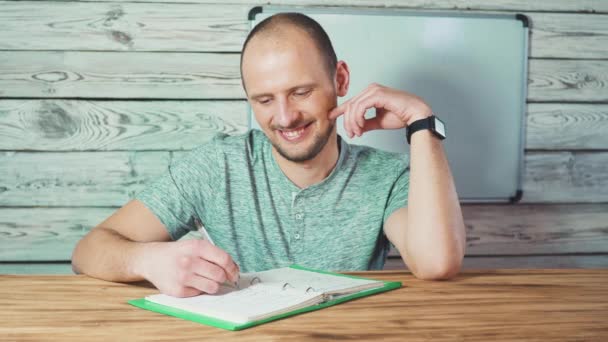 En tankefull, skjeggete fyr som skriver med notatblokk-ideer, drømmer om en mannlig student i øyeklær som ser bort og noterer . – stockvideo
