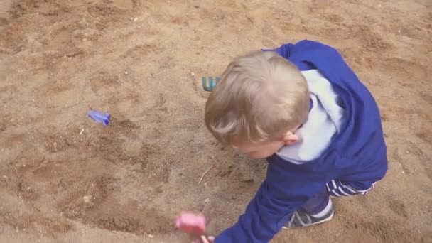 Juegos para niños. Niño cavando en la caja de arena. Sonríe y toca la arena . — Vídeo de stock