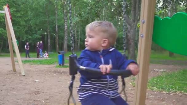 Garçon de deux ans monte sur une balançoire dans le parc — Video