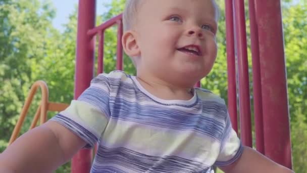 Ein fröhlicher kleiner Junge zog vom Hügel auf den Spielplatz. Kind spielt auf Spielplatz und rollt den Hügel hinunter. Zeitlupe. — Stockvideo