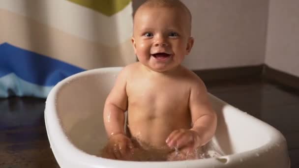 Neugeborenes Baby ist mit Wassertropfen bedeckt, spielt und lächelt in der Badewanne — Stockvideo