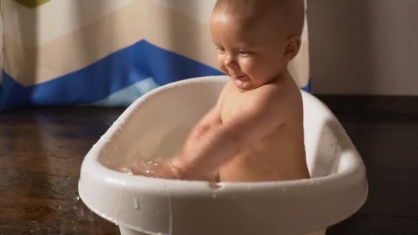 Neugeborenes Baby ist mit Wassertropfen bedeckt, spielt und lächelt in der Badewanne — Stockvideo