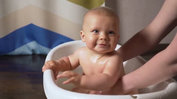 Новорожденный ребенок покрыт капли воды крупным планом играя и улыбаясь в ванне — стоковое видео