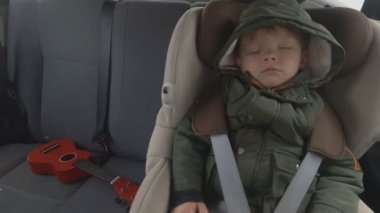 Arabanın arka koltuğunda küçük bir çocuk. Araba kötü bir yola gidiyor. Bebekle seyahat. Bir gitar ile uyuyan çocuk.