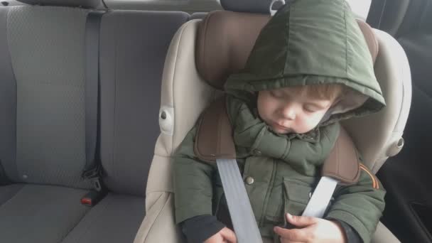 El niño en el asiento trasero de un auto está durmiendo. El coche va por un mal camino. Viajar con bebé — Vídeo de stock