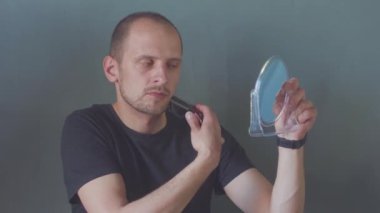 Siyah gömlekli genç adam sakalını buduyor.