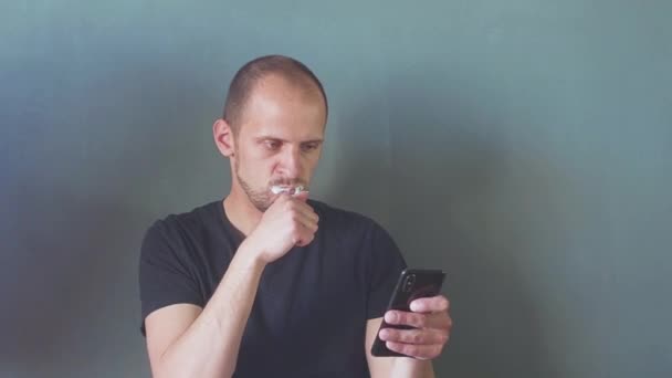 Закрыть человека с помощью смартфона. концепция телефонной зависимости. молодой бизнесмен печатает и просматривает соцсети на телефоне, чистя зубы. Hd — стоковое видео