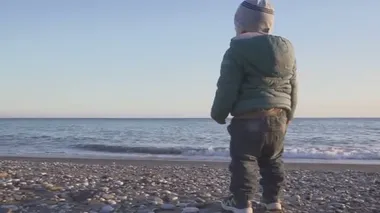 Bir yaşındaki bir bebeğin yaşam tarzı. Çocuk gün batımında denize koşar. tatil konsepti. Ağır çekim. Stedicam ile çekim