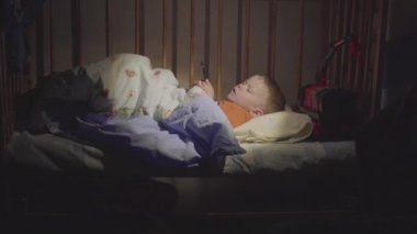 3 yaşında bir çocuk gece yatakta akıllı bir telefonla çizgi film izliyor..
