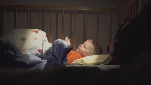 3 years old child boy using smartphone at night in bed — Stock Video