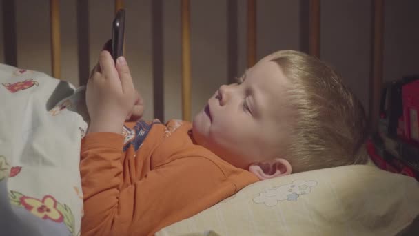 3 anos de idade criança boywatching desenhos animados em um smartphone à noite na cama . — Vídeo de Stock