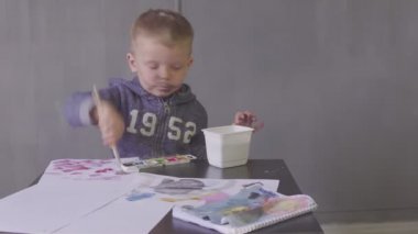 Kesik yüzlü komik bir çocuk renkli boyalarla resim çiziyor.