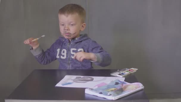 Egy gyerek vicces fiú megvágott arccal színes festékkel rajzol. — Stock videók