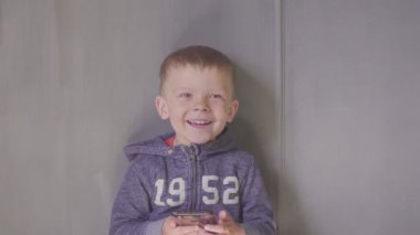 Akıllı telefonlu, çizgi film seyreden, gülümseyen ve gülen tatlı bir oğlan çocuğu.