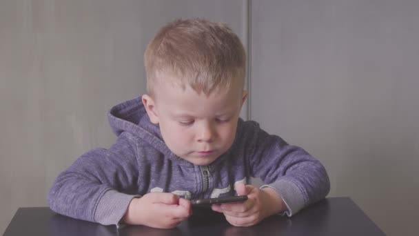 Ung söt liten pojke med smartphone titta på karikatyrer, ler och skrattar — Stockvideo