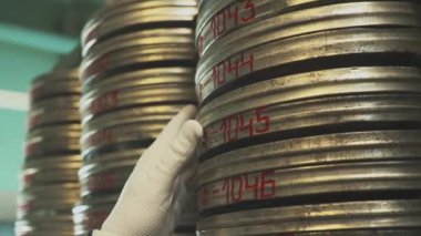 Büyük film arşivlerinde eski filmlerin olduğu metal kutular. Beyaz eldivenli bir arşivcinin elleri doğru filmi arıyor..