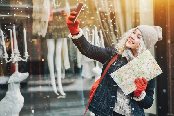Sonriente chica rubia rizada con mapa haciendo selfie, invierno —  Fotos de Stock