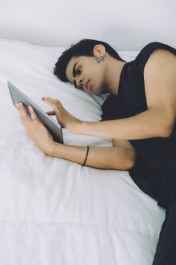 Brazilian guy laying on the bed with digital tablet clipart