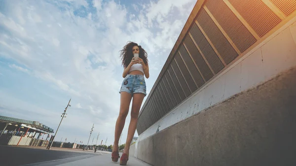 Young curly hipster brunette girl walking with smartphone — Stock Photo, Image