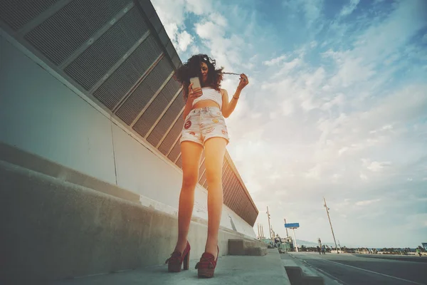 Curly attractive girl standing and using her smartphome — Stock Photo, Image