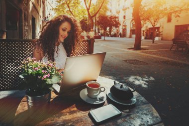 Sokak kafede dizüstü bilgisayar üzerinde çalışan kıvırcık esmer kız