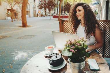 Kafede dizüstü bilgisayar üzerinde çalışan kıvırcık gülümseyen güzel kız