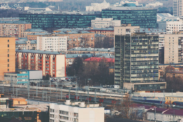 Close-up shooting from top of metropolitan city: several tracks of railway with suburban electric train, residential and business office buildings and districts, multiple facades, Moscow, Russia