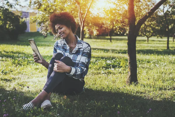 デジタル タブレットの公園で座っていると黒の女の子 — ストック写真
