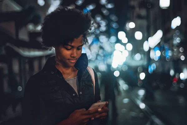 Chica birracial rizado con teléfono inteligente en la calle de la ciudad de noche — Foto de Stock