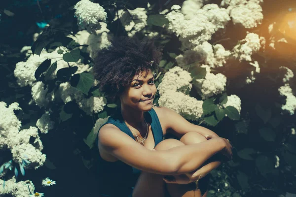 Vrolijke zwarte meisje voor muur van witte bloemen — Stockfoto