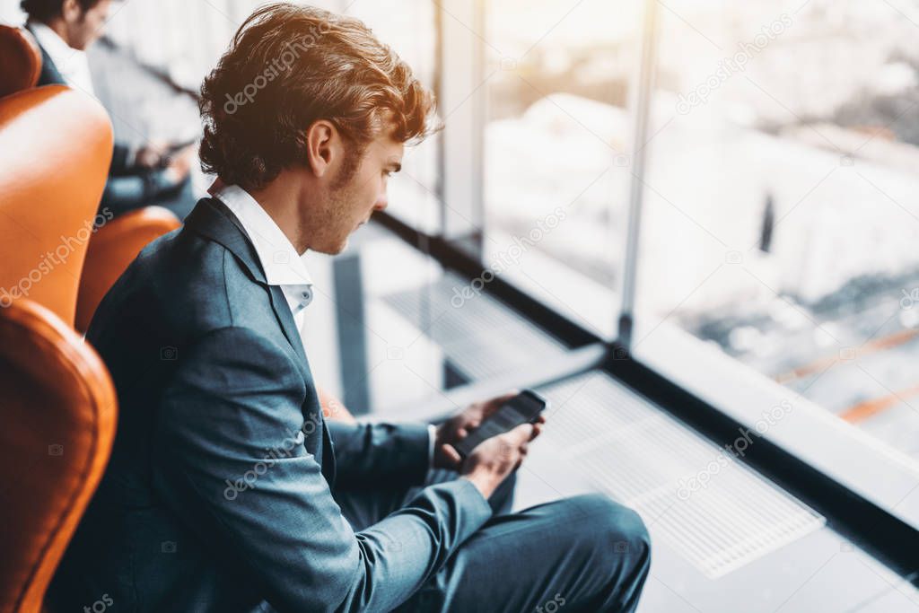 Businessman with smartphone in office with reflections and windo
