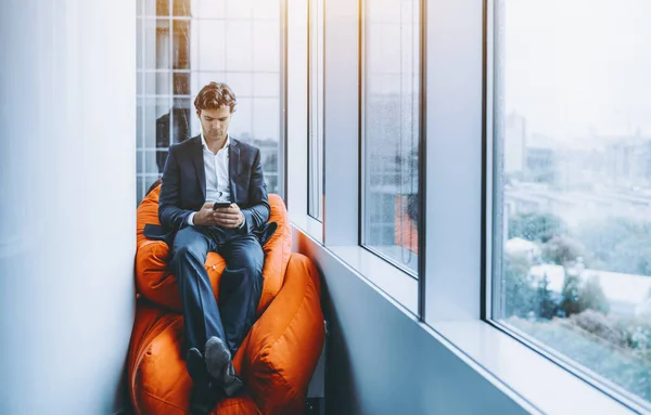 Бизнесмен отдыхает со смартфоном на оранжевых подушках — стоковое фото