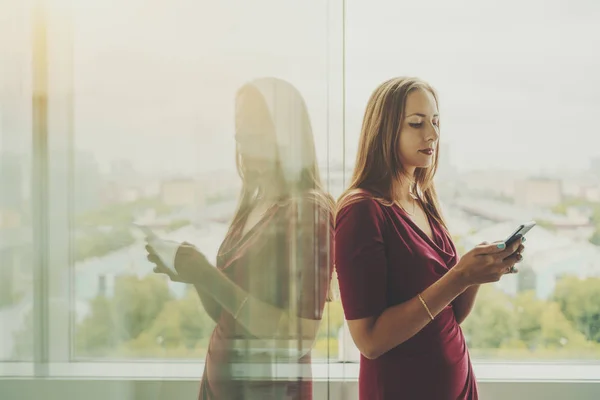 Femme d'affaires en robe rouge avec téléphone portable près de la fenêtre — Photo