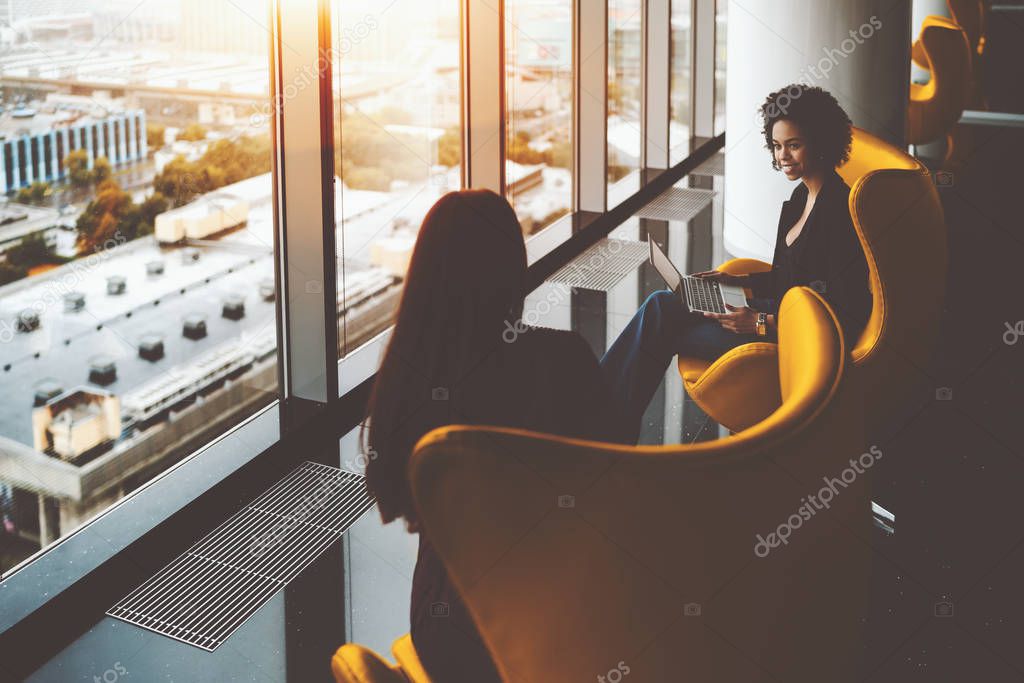 Two businesswomen having work meeting near office windows