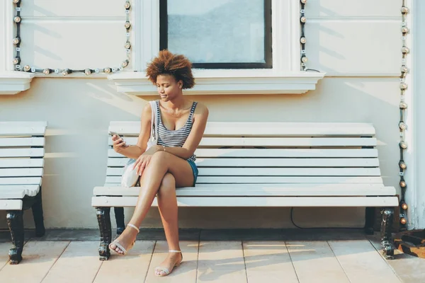 手机在街头长椅上的黑人年轻女子 — 图库照片
