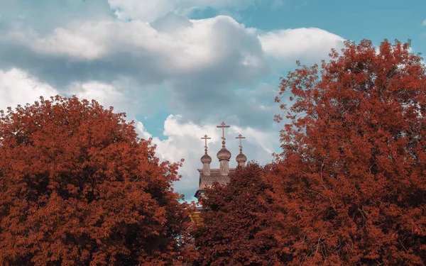 Igreja de madeira atrás de árvores vermelhas de outono — Fotografia de Stock