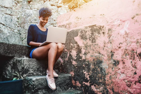 Black smiling girl with laptop on stone staircase — Stock Photo, Image
