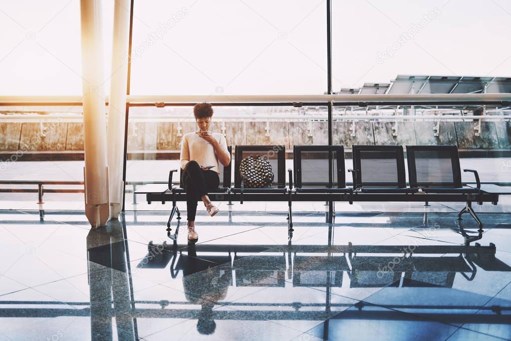 Black girl using cellphone in waiting hall of airport