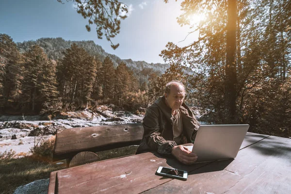 Old hunter with his laptop in mountains