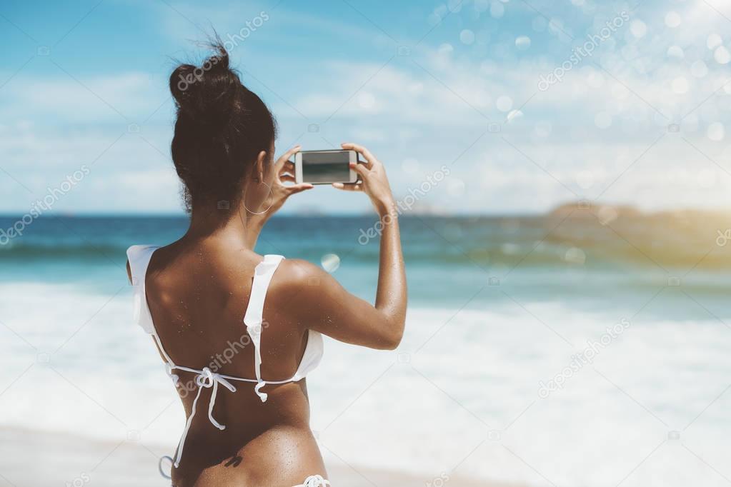 Rear view of black girl taking pictures on the beach
